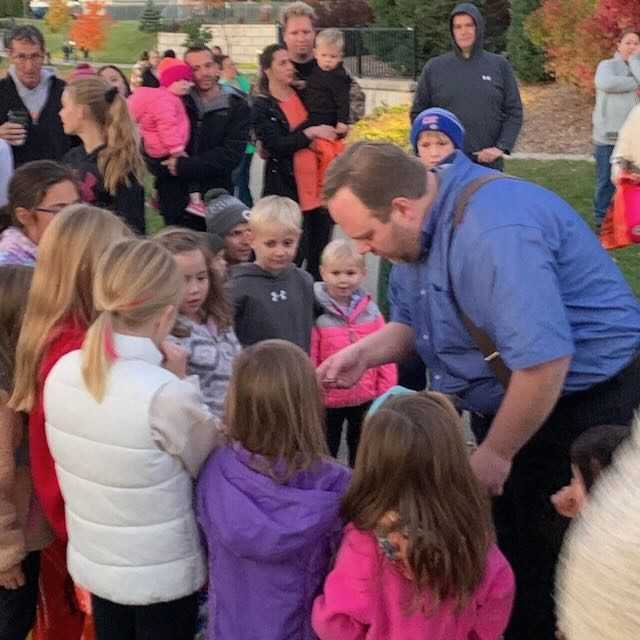Children pressed in close around Hanneman for close-up magic outdoors